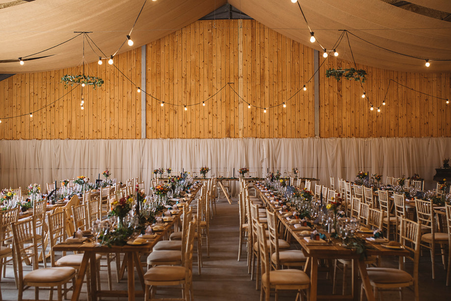 Long tables for wedding meal decorated with colourful flowers and lights hanging above